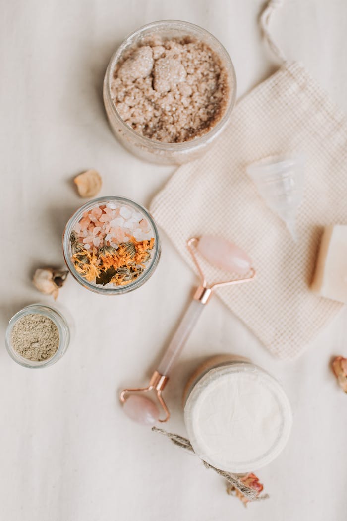 Aesthetic flat lay of bath products including a jade roller, bath salts, and natural soaps.
